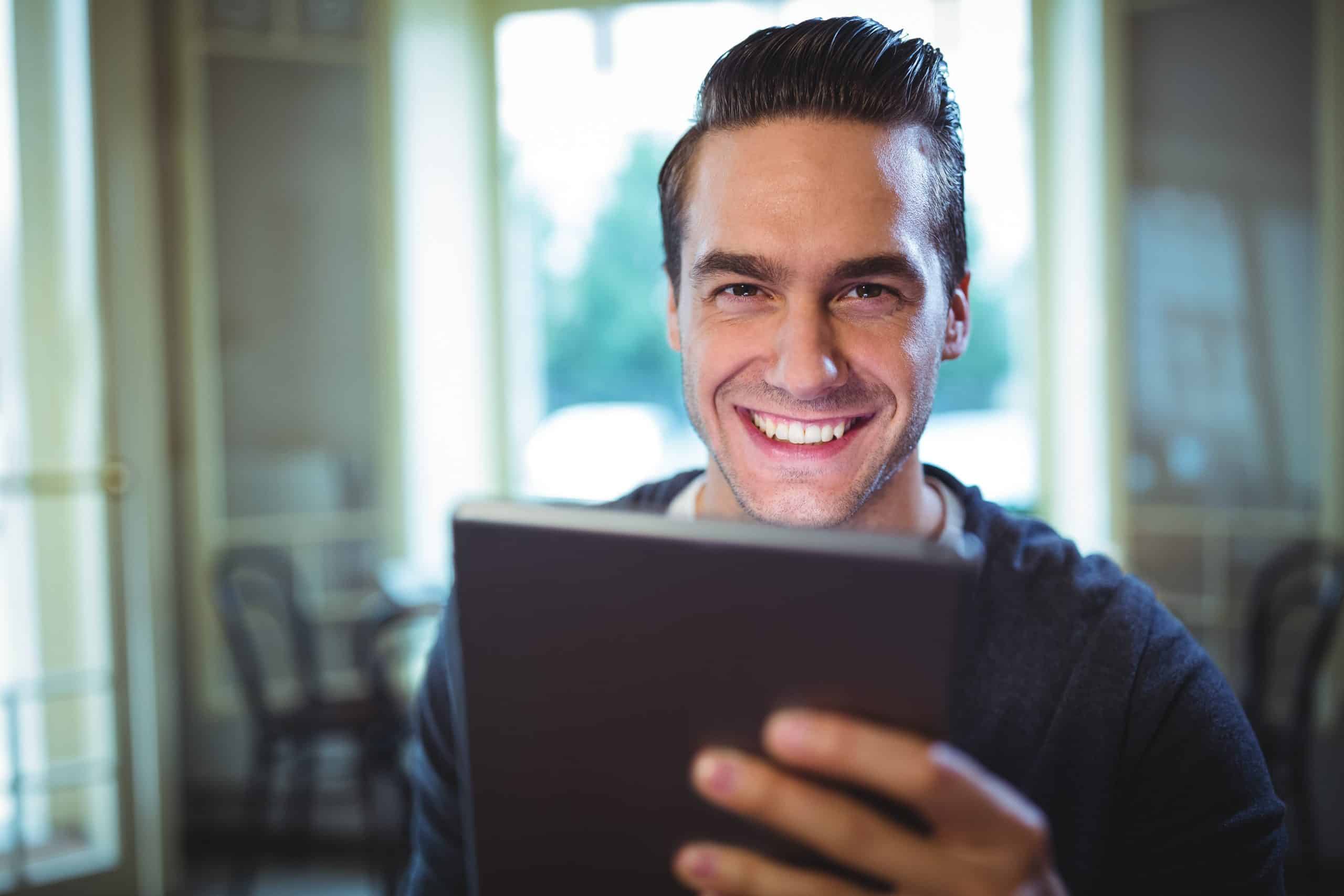 A man is smiling while using a tablet computer.