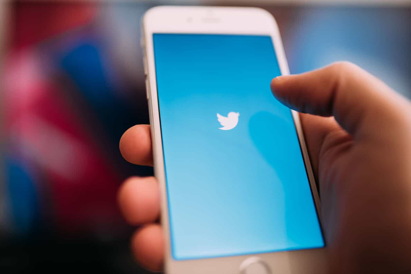 A person holding an iphone with the twitter logo on it.